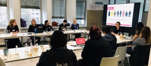 Foto von Vortragender Dr. Sandra Buchmüller und Zuhörenden um Konferenztisch. Im Hintergrund Powerpoint des Vortrags „Moderne Ansätze für Gender und Diversity in der Technikgestaltung und ihre Verbreitung‟